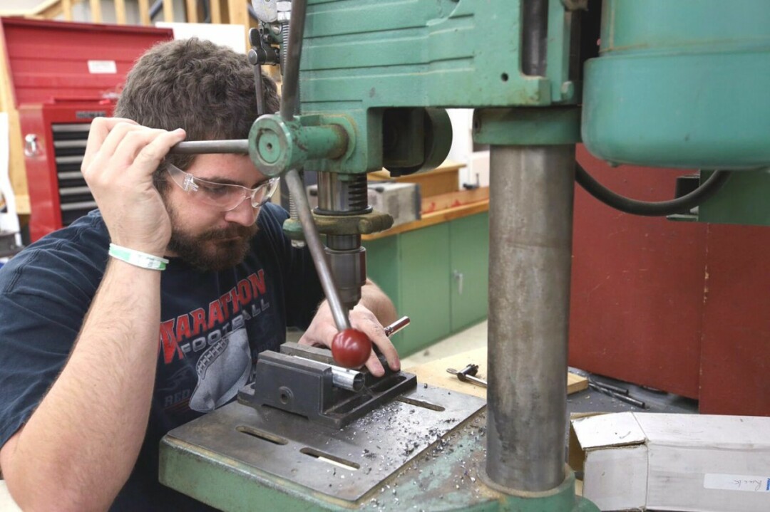 Engineering student Cole Bergman uses a drill press while working on the Buvala Fence Cart.
