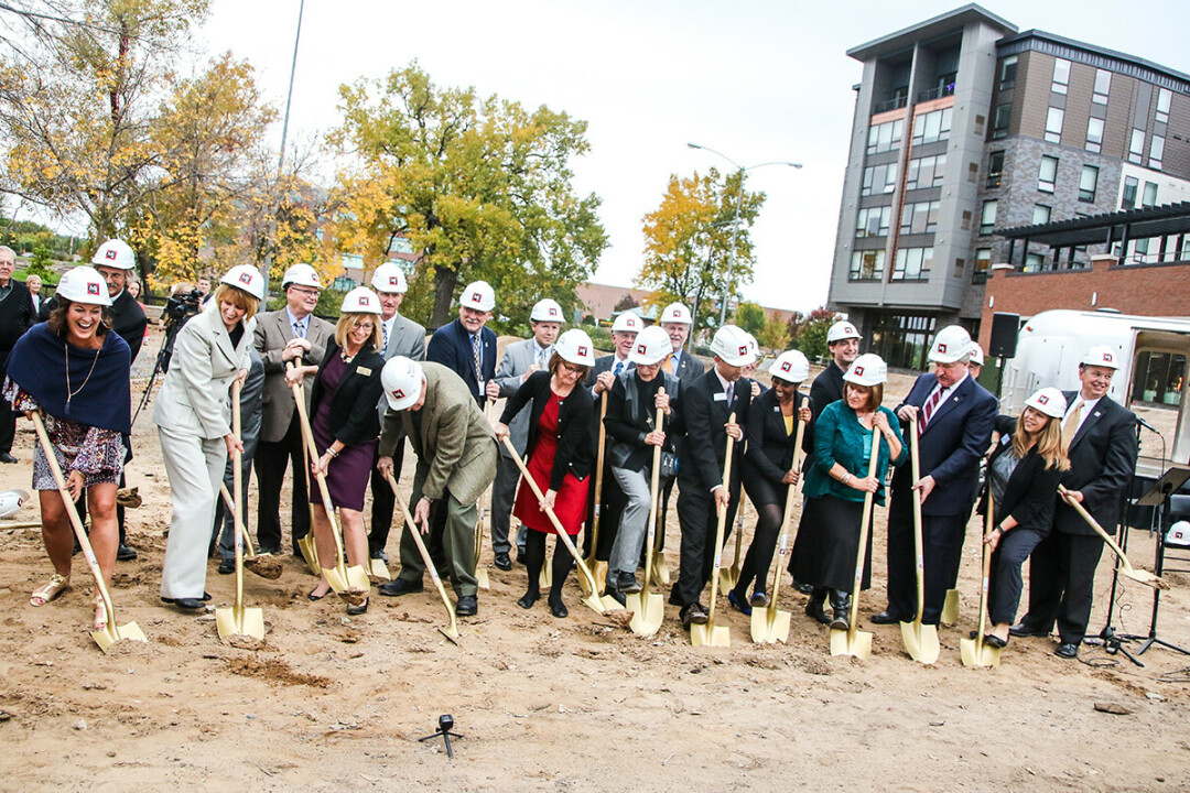 Mike Rindo (standing in the back row wearing a navy blue blazer) takes part in a groundbreaking for the Confluence Project in downtown Eau Claire in October 2016. (Photo by Andrea Paulseth)
