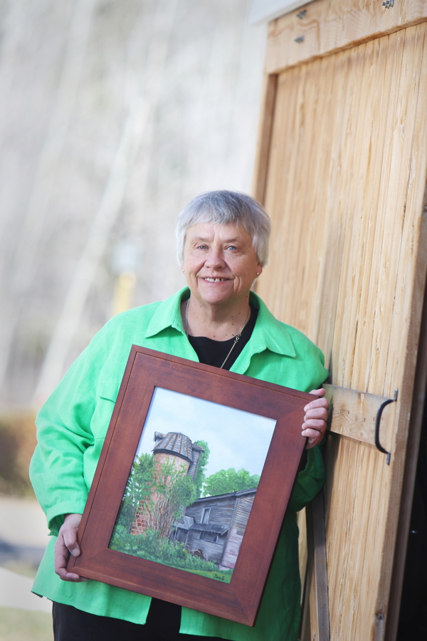 Framing a good story. Local author Jane Glenz’s new novel is called The Moore Farm Secret. The picture Glenz is holding depicts the real-world farm portrayed in the book.
